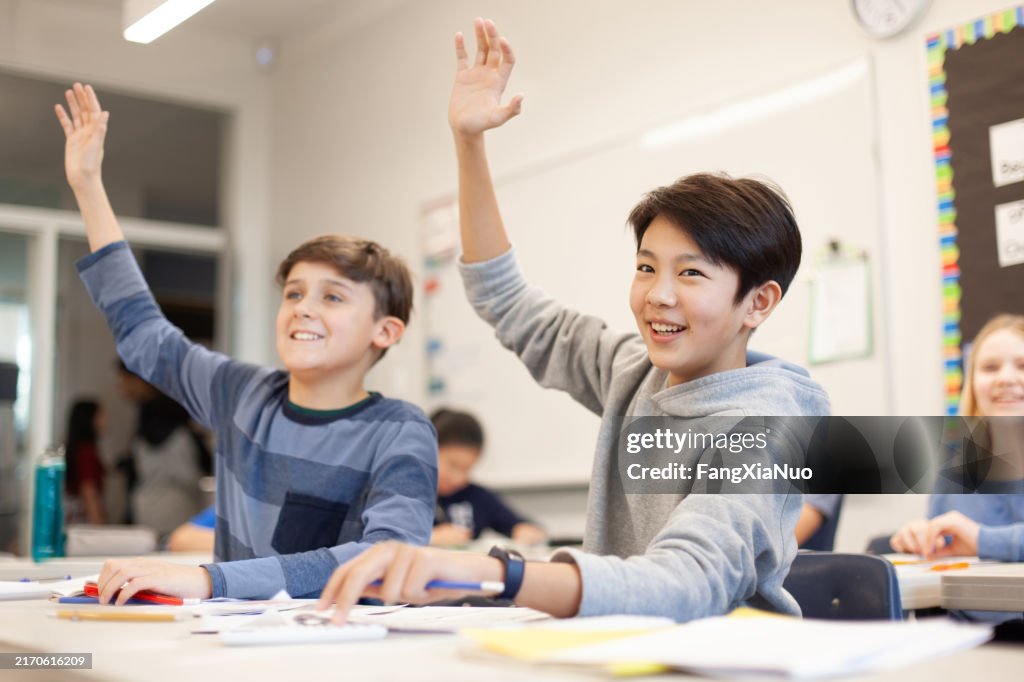 Portrait of Asian Japanese Korean multiracial junior high elementary school student boy raising hand to answer question in classroom with classmates