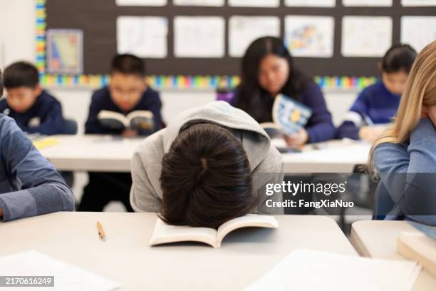 grundschule junior high boy schüler sitzt am schreibtisch im klassenzimmer mit kopf im buch in frustration schlaf müde erschöpfung langeweile - hoffnungslosigkeit stock-fotos und bilder