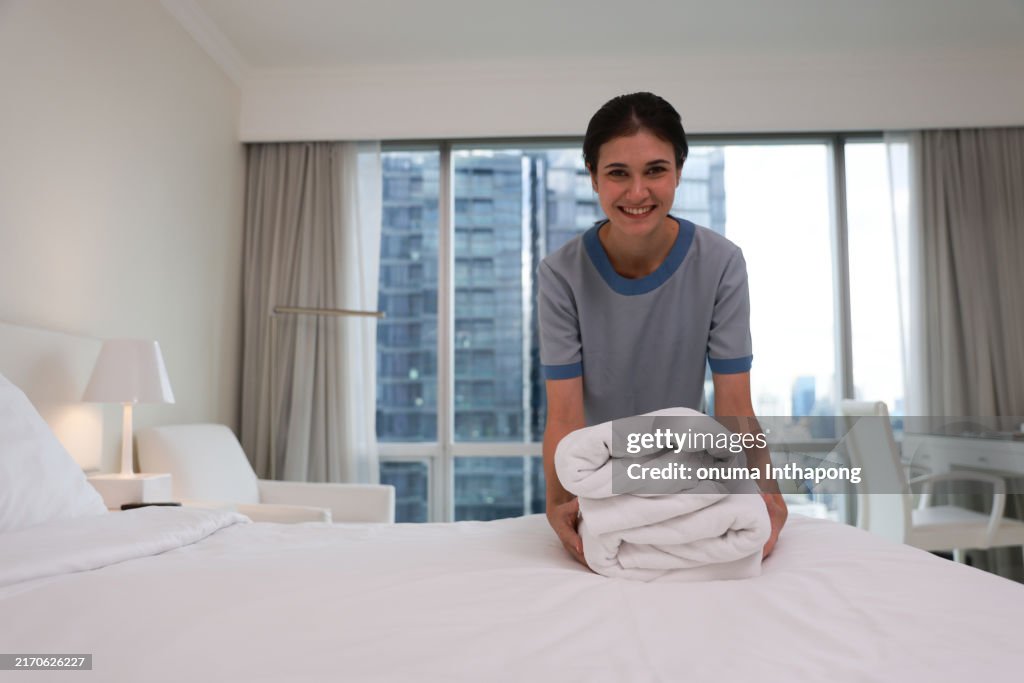 A happy maid working at a hotel and changing the towels,Housekeeper working at a hotel changing the towels in a room