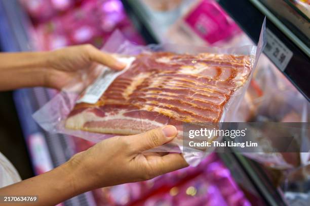 una foto recortada de una mujer seleccionando cuidadosamente tocino de cerdo crudo en la sección de carne procesada de un supermercado. - tocino ahumado fotografías e imágenes de stock