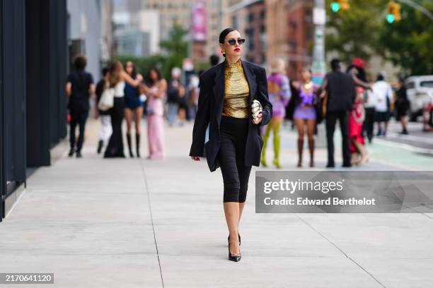 Guest wears black sunglasses, gold earrings, shiny gold high neck shirt, black oversized blazer jacket, black capri pants, gold handbag, shiny black...