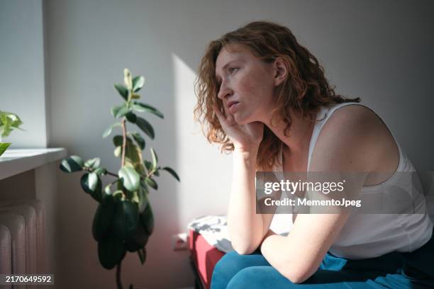 sad depressed woman sitting on bed touching head suffering from headache. migraine symptoms - coeur brisé photos et images de collection