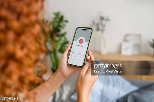 woman activating home security system on smartphone app while relaxing at home - iphone camera interface stock pictures, royalty-free photos & images