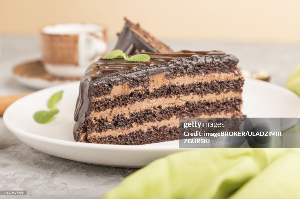 Homemade chocolate cake with milk cream and a cup of coffee on a gray concrete background with green textile. side view, close up, selective focus