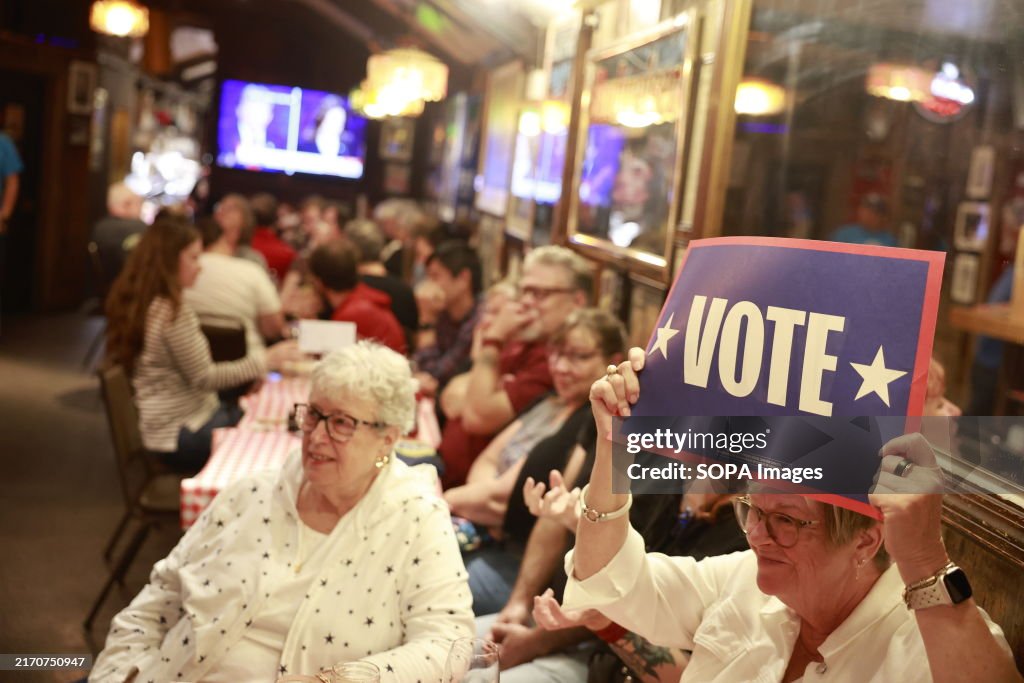 A woman holds a "Vote" placard while watching the...
