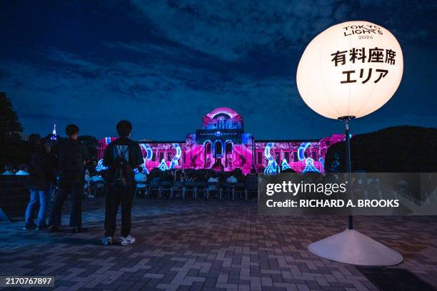 People watch a special projection mapping chosen from a competition as it is displayed against the exterior of the Meiji Memorial Museum during a...