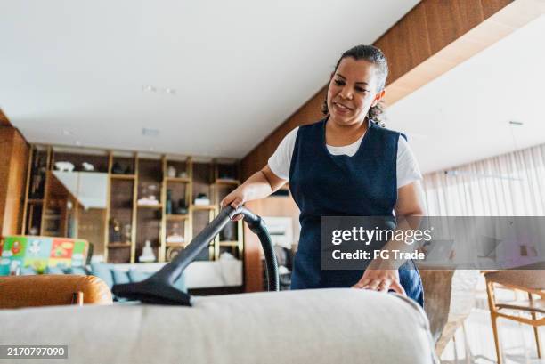 housekeeper vacuuming sofa in a house - schoonmaakpersoneel stockfoto's en -beelden