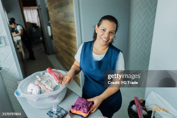 portrait d’une femme de ménage organisant des vêtements pour bébés dans une maison - agent de ménage photos et images de collection