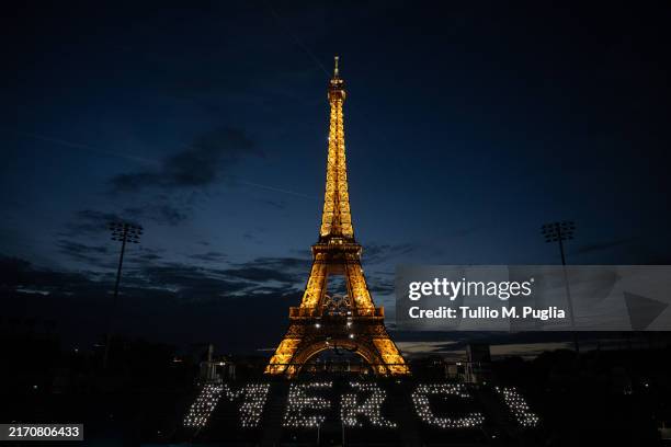 In this image released on September 8, a number of Paris 2024 staff and volunteers gather at night fall in the Eiffel Tower Stadium to send a...