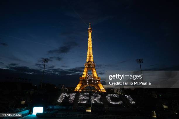 In this image released on September 8, a number of Paris 2024 staff and volunteers gather at night fall in the Eiffel Tower Stadium to send a...