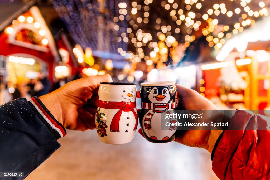 Two persons drinking Glühwein (Mulled Wine) from snowman and penguin shaped Christmas market in Berlin, Germany