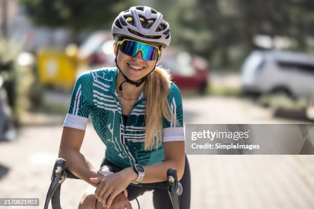 portrait of a young female racer on a road bike. a caucasian young woman standing with bike, wearing cycling equipment and looking at the camera. - bicicleta de corrida imagens e fotografias de stock