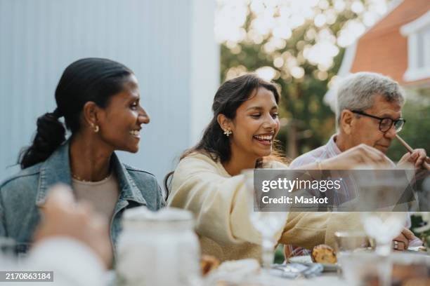 cheerful teenage girl having lunch with family members during social gathering at garden party - sociale bijeenkomst stockfoto's en -beelden