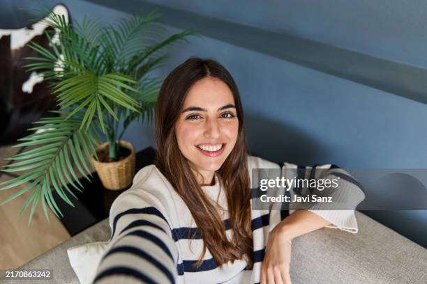 woman happily smiles while taking a selfie on her cozy sofa at home. radiating positivity and joy - cozy home stock pictures, royalty-free photos & images
