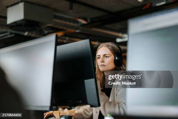 focused female entrepreneur with wireless headphones doing coding on computer in office - concentration stock pictures, royalty-free photos & images