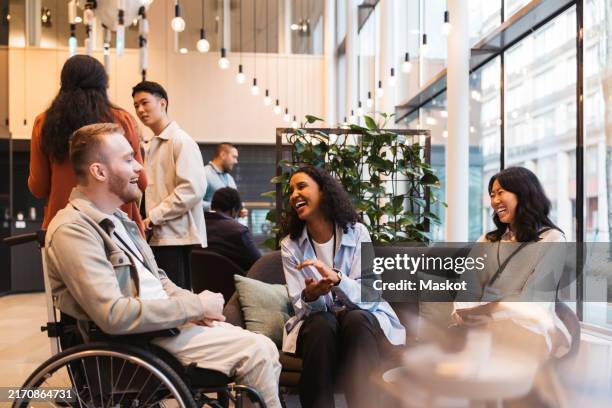 happy businesswomen discussing with male entrepreneur sitting on wheelchair at convention center - igualdad fotografías e imágenes de stock