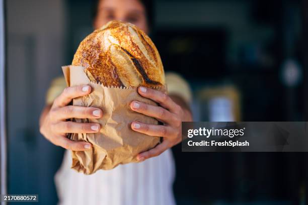 baker holding fresh artisan bread in paper bag - bakery stock pictures, royalty-free photos & images