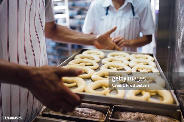 bäcker, die in einer bäckerei frisch gebackene brezeln zubereiten - breze stock-fotos und bilder