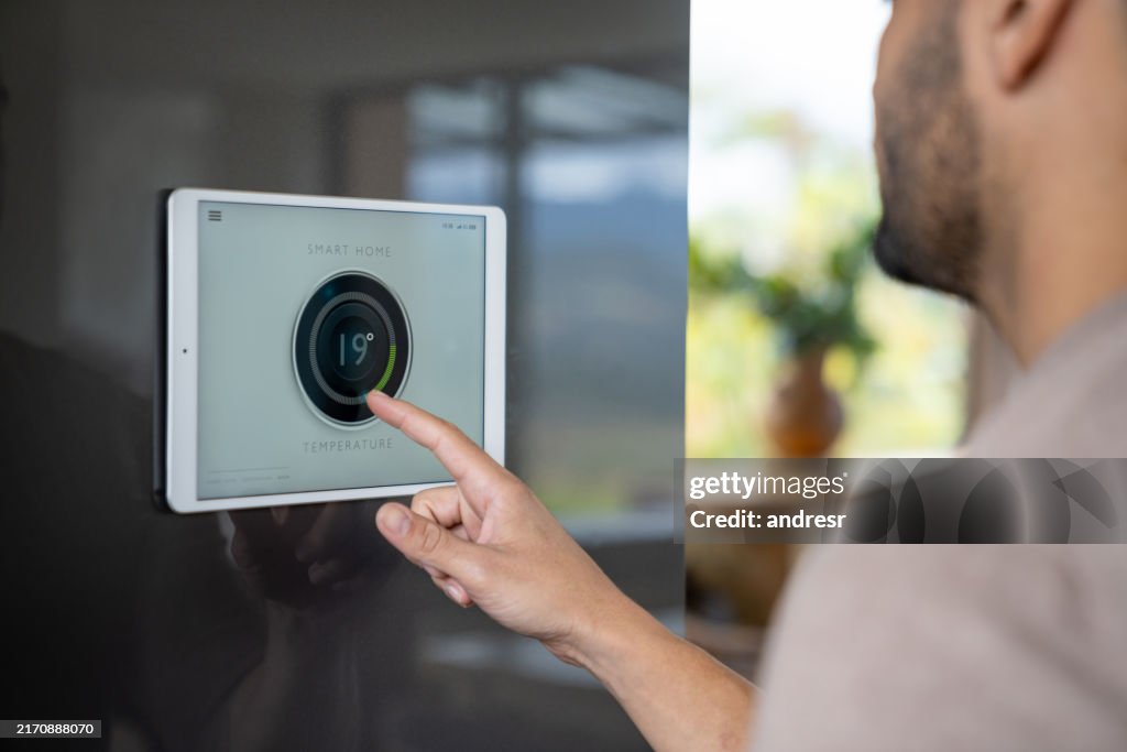 Mann zu Hause, der die Temperatur mit seinem intelligenten Thermostat kontrolliert