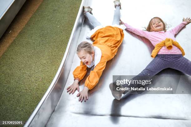 friendship and fun: two happy kids girls sliding together at the park playground - kid sliding stock pictures, royalty-free photos & images