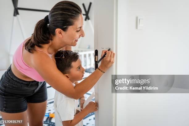 happy mother measuring son's height on door - growth chart stock pictures, royalty-free photos & images