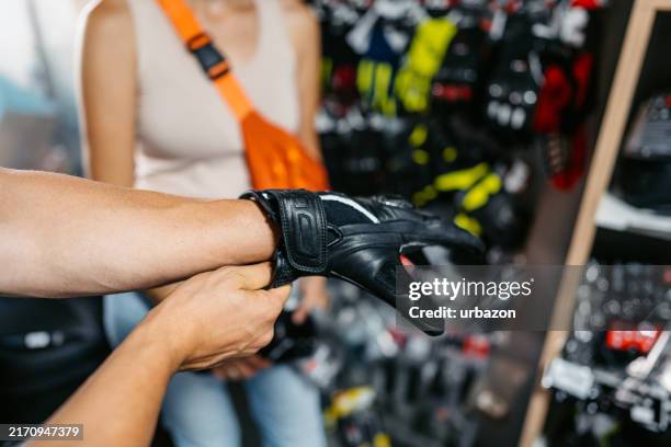 jeune homme essayant des gants de moto dans un magasin de moto - gants de sport photos et images de collection