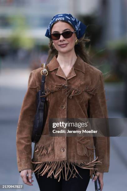 Guest seen wearing a blue pattern bandana headband, gold round earrings, DMY Studios black oval sunglasses, vintage brown suede leather jacket with...