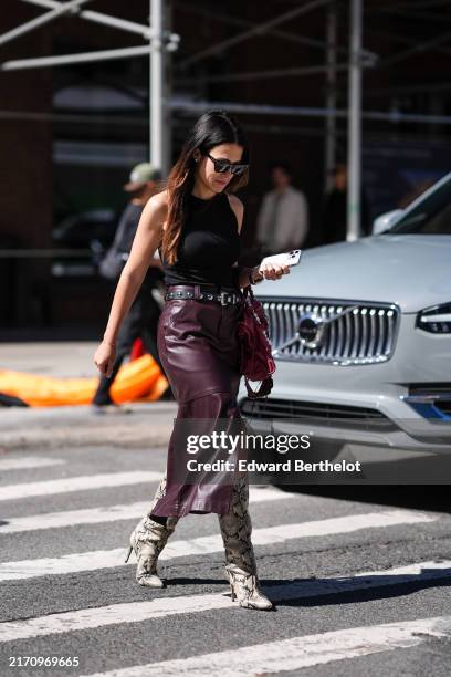 Guest wears black sunglasses, black sleeveless shirt, black leather silver studded belt, dark red / burgundy brown leather midi skirt, dark red...
