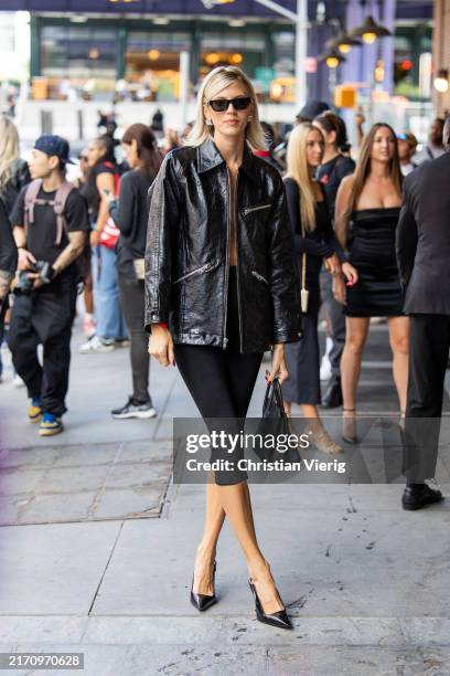 Devon Windsor wears black vinyl jacket, capri pants, bag outside Alexander Wang New York Fashion Week on September 08, 2024 in New York City.