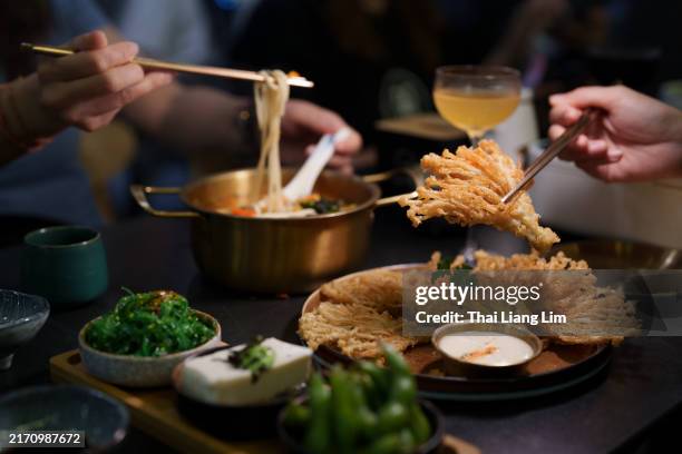 une vue rapprochée des personnes dégustant un dîner végétarien, composé de champignons enoki frits croustillants et d’un bol de nouilles ramen dans un restaurant végétarien confortable. - cuisine japonaise photos et images de collection