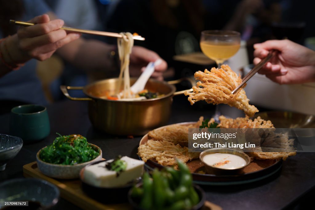 A close-up view of people enjoying a vegetarian dinner, featuring crispy deep-fried enoki mushrooms and a bowl of ramen noodles in a cozy vegetarian restaurant.
