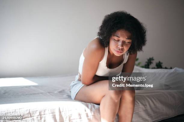 pms symptoms. young african american woman touching belly suffers from stomachache at home - verstopt stockfoto's en -beelden
