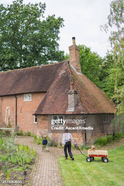 mother pulls child in wagon outside of country cottage - english architecture stock pictures, royalty-free photos & images