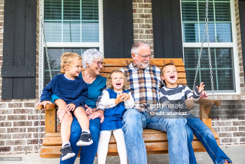 Grandparents laughing and playing on a porch swing out in the country