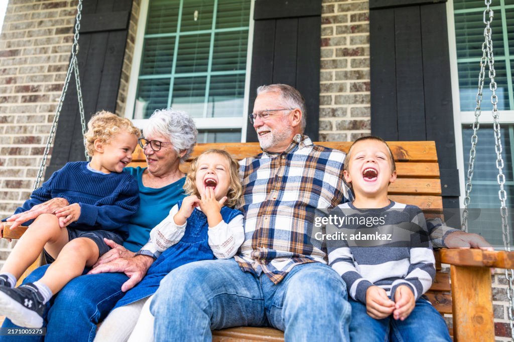 Grandparents laughing and playing on a porch swing out in the country