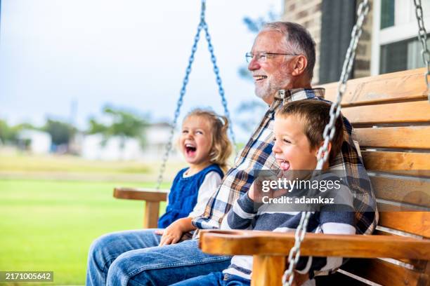 divertida hora del cuento con el abuelo en el columpio del porche - familia multigeneracional fotografías e imágenes de stock