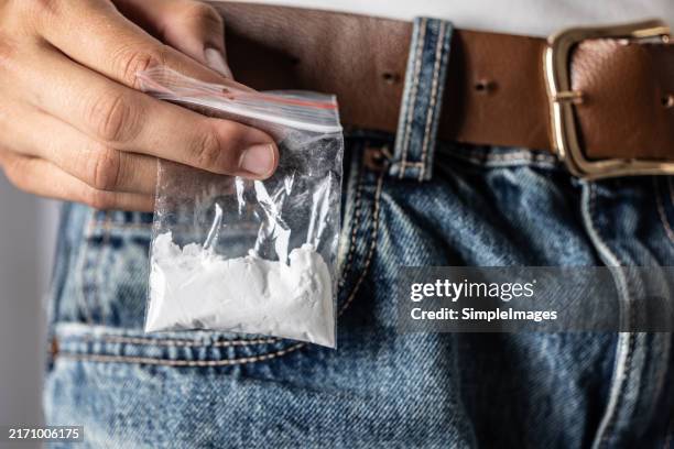 the hand selects a package with a drug - cocaine in the back pocket of jeans - drogue à usage récréatif photos et images de collection