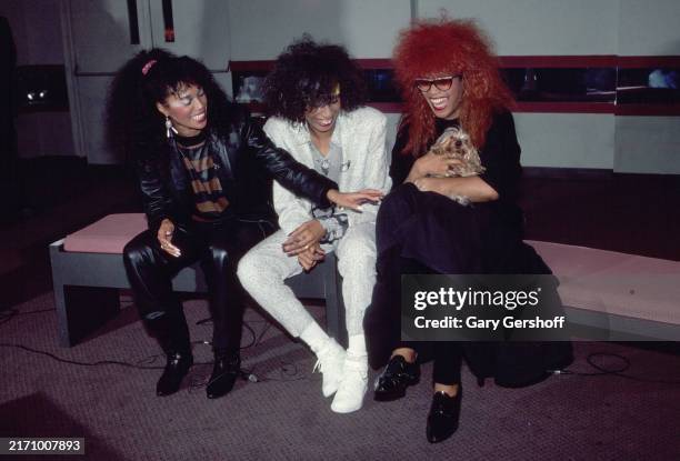 View of members of American R&B, Pop, & Disco group the Pointer Sisters, seated on a bench backstage, prior to their performance at the Westbury...