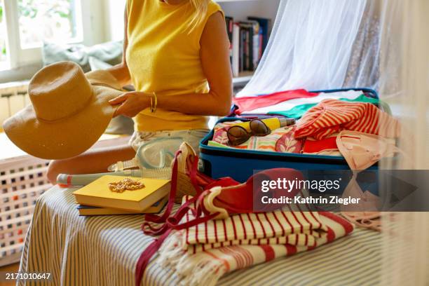 woman sitting on bed, packing suitcase for summer holidays - imballare foto e immagini stock