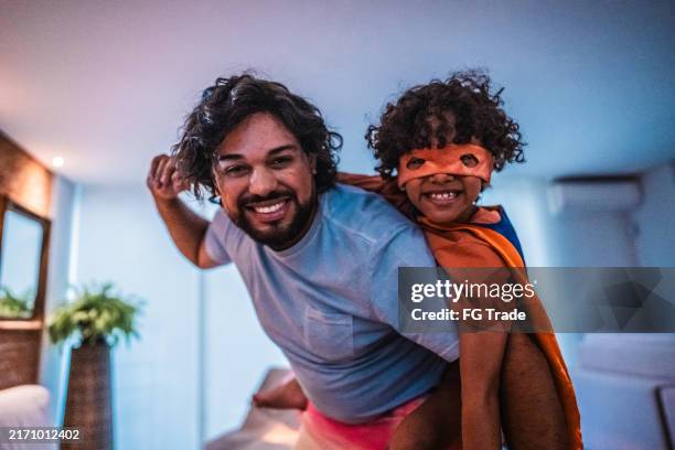 portrait of father carrying superhero son on his back playing at home - dad superhero stock pictures, royalty-free photos & images