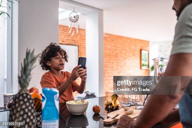 boy fiming father preparing smoothie at home - social media followers stock pictures, royalty-free photos & images