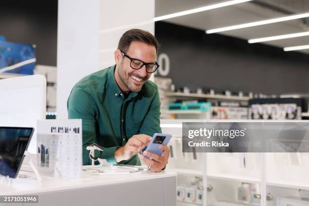 a customer browsing the latest smart phone models in a store - electronics store stock pictures, royalty-free photos & images