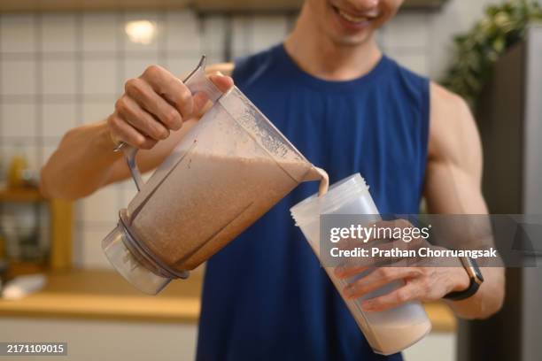 young sporty man pouring a freshly blended chocolate protein shake from a blender into a shaker bottle. - eiwit organische verbinding stockfoto's en -beelden