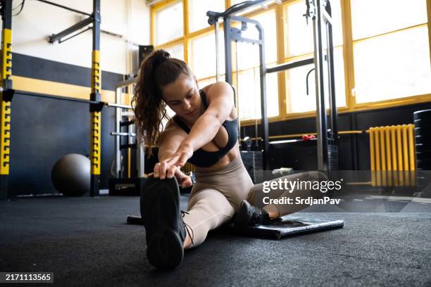 young caucasian female athlete stretching her body in the gym - warm up exercise stock pictures, royalty-free photos & images
