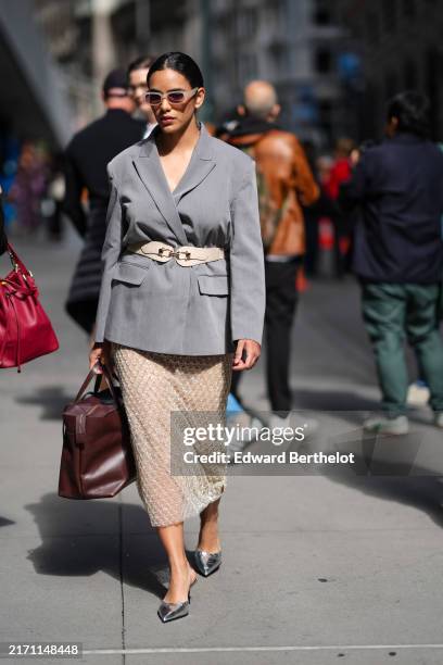 Guest wears white sunglasses, light gray oversized blazer jacket, white belt, white sheer mesh beaded midi skirt, shiny dark brown leather bag, shiny...