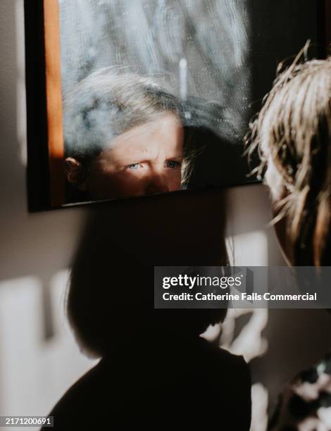 young child gazes intently into a mirror reflecting their expression in a softly lit room during the afternoon - trotzanfall stock-fotos und bilder