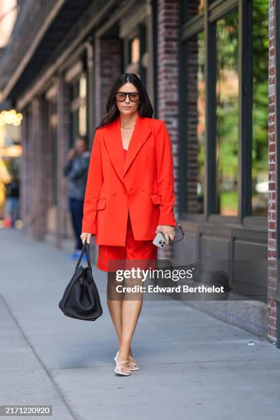 Guest wears black sunglasses, silver necklace, bright red oversized blazer jacket, bright red over the knee shorts, shiny black The Row leather tote...
