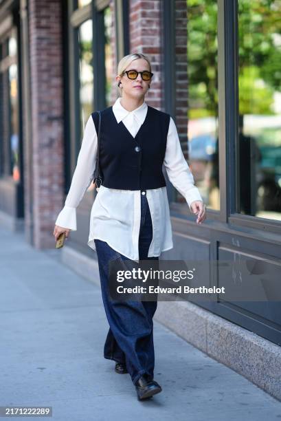 Guest wears black sunglasses, black earrings, white button up long sleeve shirt, black cropped sweater vest, navy blue denim jean baggy pants, black...