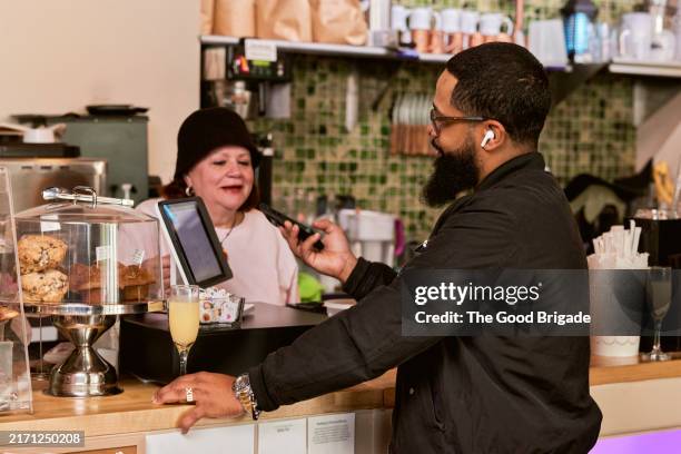 male customer talking with senior woman at checkout in cafe - in ear headphones stock pictures, royalty-free photos & images