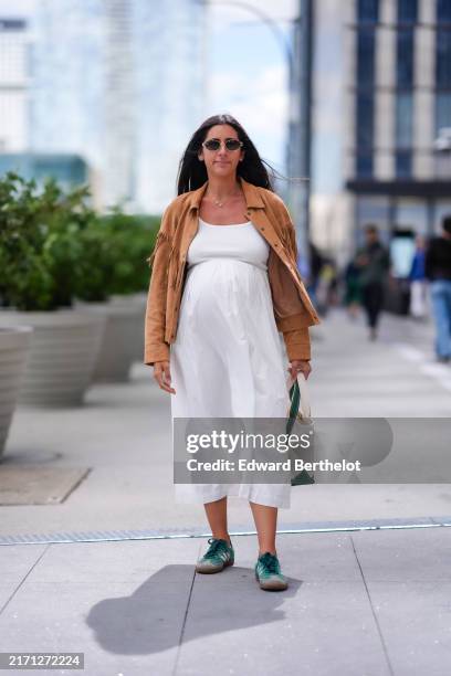 Guest wears black sunglasses, silver necklace, white midi dress, light brown suede tassel jacket, dark green Adidas Originals Samba sneaker shoes,...